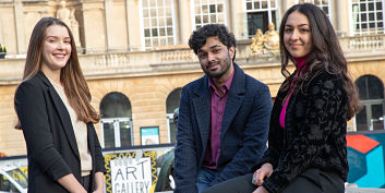 three smiling students outside a university building in Bristol, from lef to right, female, male, female.